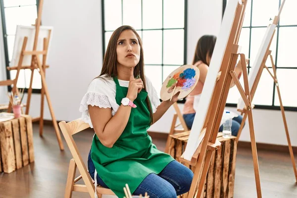 若いヒスパニックなアーティストの女性は アートスタジオでキャンバスに絵を描く思考は顎に指で疑いに集中し 疑問を検索 — ストック写真