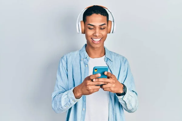 スマートフォンを使っている若いアフリカ系アメリカ人の男は 前向きな笑顔で立って笑顔で歯を見せています — ストック写真