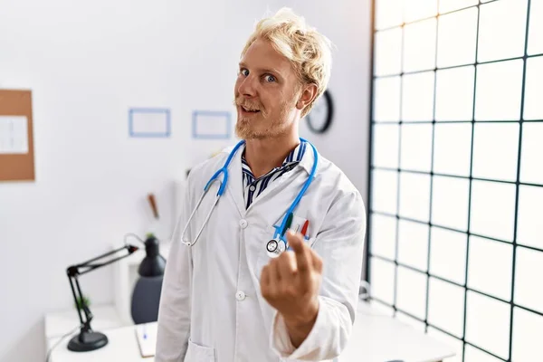 Jonge Blonde Man Doktersuniform Stethoscoop Kliniek Wenkend Kom Hier Gebaar — Stockfoto