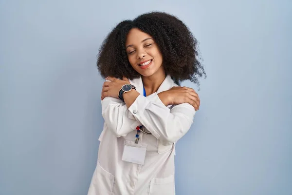 年轻的非洲裔美国女人穿着医生制服和听诊器 幸福而积极地拥抱自己 充满自信地微笑 自爱和自我照顾 — 图库照片