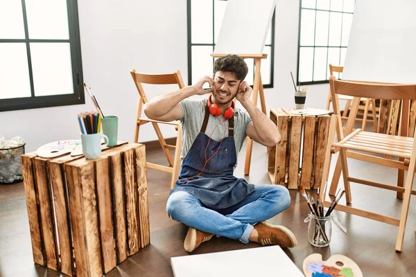 Young Hispanic Man Sitting Art Studio Covering Ears Fingers Annoyed — стоковое фото
