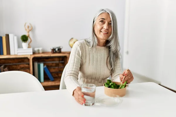 中年白髪の女性家庭でテーブルの上に座ってサラダを食べる — ストック写真