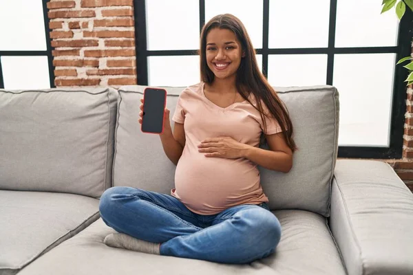 Młoda Ciężarna Kobieta Trzyma Smartfon Pokazując Ekran Patrząc Pozytywnie Szczęśliwy — Zdjęcie stockowe