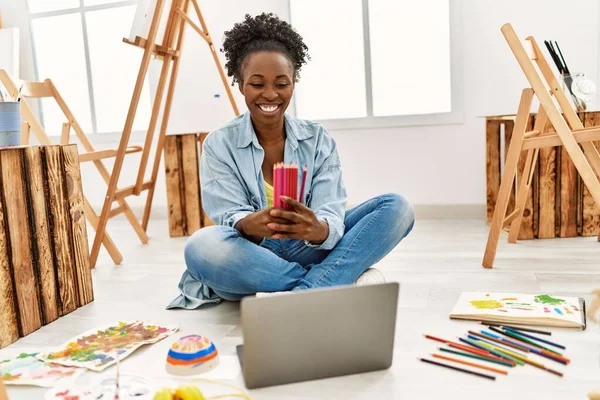 年轻的非洲裔美国女艺术家用笔记本电脑在艺术工作室里拿着彩色铅笔 — 图库照片