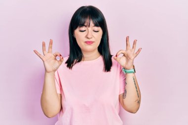 Gündelik kıyafetler giyen, gözleri kapalı gülümseyen genç İspanyol kadın parmaklarıyla meditasyon hareketi yapıyor. yoga konsepti. 