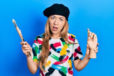 Kafkasyalı genç bir kadın sanatçı elinde küçük tahta manikin ve şok olmuş yüzünde boya fırçaları tutuyor. Şüpheci ve alaycı görünüyor, ağzı açık kalınca şaşırıyor. 