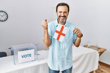 Siyasi seçim kampanyasında sakallı orta yaşlı bir adam İngiltere bayrağını tutarak gururla haykırıyor, zaferi ve başarıyı kutluyor. 