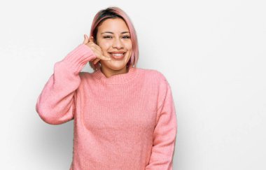 Pembe saçlı, sıradan bir süveter giyen İspanyol kadın telefonla el ve parmak hareketi yaparak telefonda konuşur gibi gülümsüyor. iletişim kavramları. 