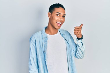 Genç, Afro-Amerikalı, günlük kıyafetler giymiş, gülümseyen, gülümseyen ve başparmağıyla yan tarafı gösteren adam.. 