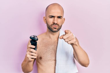 Tişörtsüz, elinde elektrikli jiletle kameraya doğru bakan genç kel bir adam ve sen kendine güvenen ciddi görünüyorsun. 