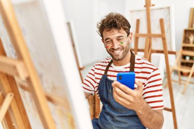 Genç İspanyol adam resim stüdyosunda akıllı telefon çizimi yapıyor.