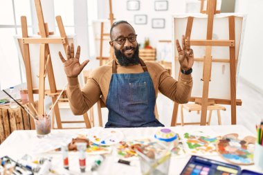 African american artist man at art studio showing and pointing up with fingers number eight while smiling confident and happy. 