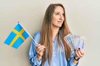 Elinde İsveç bayrağı ve Krone banknotları olan genç sarışın kadın gülümsüyor ve başka tarafa bakıyor.. 