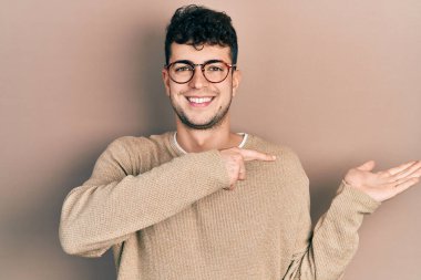 Gündelik kıyafetler giyen ve gözlüklü genç İspanyol adam kameraya hayret ediyor ve gülümsüyor.. 