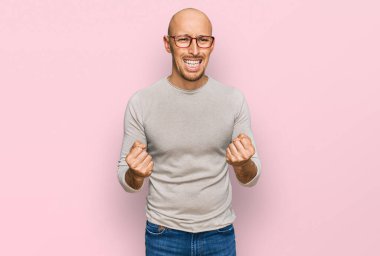 Kel, sakallı, günlük kıyafetler giyen, gözlüklü, mutlu ve heyecanlı bir şekilde kolları havada, gülümseyen ve başarı için bağıran kazanan bir jest yapıyor. kutlama konsepti. 