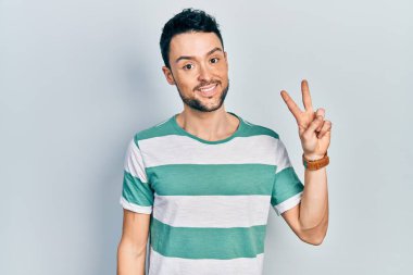 Gündelik kıyafetler giyen genç İspanyol adam iki numarayı gösterip işaret ederken kendinden emin ve mutlu bir şekilde gülümsüyor.. 