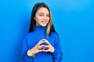 Balıkçı yaka kazak giyen genç esmer kız ellerini birleştirip gülümseyerek gevşemiş ve neşeli olmasını diliyordu. Başarı ve iyimserlik 