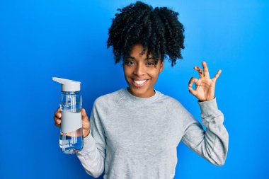 Afro saçlı Afrikalı Amerikalı kadın bir şişe su içiyor parmaklarıyla işaret veriyor, gülümseyerek mükemmel bir sembol oluşturuyor. 