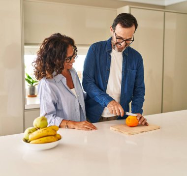 Orta yaşlı İspanyol çift gülümsüyor. Mutfakta turuncu kesiyorlar.