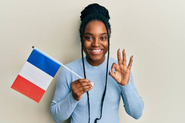 Saçları örgülü, elinde Fransa bayrağı olan Afro-Amerikalı kadın parmaklarıyla işaret veriyor, gülümseyerek mükemmel bir sembol oluşturuyor. 