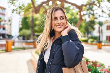 Parkta kendinden emin gülümseyen genç sarışın kadın.