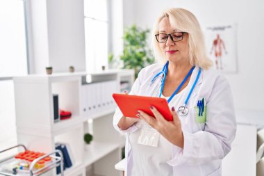 Klinikte dokunmatik ped kullanan orta yaşlı sarışın kadın.