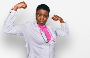 Genç Afrikalı Amerikalı kadın doktor üniforması giyiyor ve steteskop gururla gülümseyen kol kaslarını gösteriyor. fitness konsepti. 
