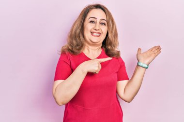 Orta yaşlı beyaz kadın, sıradan kıyafetler giyip kameraya hayret ediyor ve gülümsüyor.. 