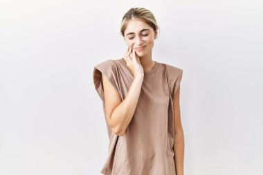 İzole edilmiş arka planda duran genç sarışın kadın diş ağrısı ya da diş hastalığından dolayı acı dolu bir ifadeyle ağıza dokunuyor. dişçi 