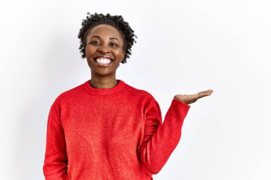 Genç Afrikalı Amerikalı kadın, izole edilmiş arka planda günlük giysiler giyip neşeli bir şekilde sunum yapıyor ve avuç içiyle kameraya bakıyor.. 