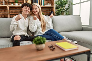 Genç ve güzel bir çift evdeki kanepede oturmuş gururla bağırıyor, zaferi kutluyor ve kollarını kaldırarak çok heyecanlanıyor. 