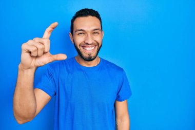 Sakallı, günlük mavi tişörtlü, gülümseyen, kendine güvenen, el hareketi yapan, parmaklarıyla işaret eden ve kameraya bakan İspanyol bir adam. ölçüm kavramı. 