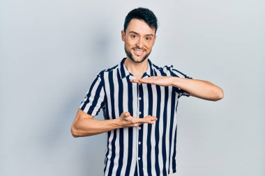 Latin asıllı genç adam, sıradan kıyafetler giyiyor. Elleriyle işaret ediyor. Ölçü sembolü, büyük boy işareti. Kameraya bakıp gülümsüyor. ölçüm kavramı. 