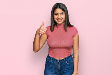 Gündelik tişört giyen genç İspanyol kız elinle mutlu bir jest yapıyor. Kameraya bakıp başarıyı gösteren ifade. 