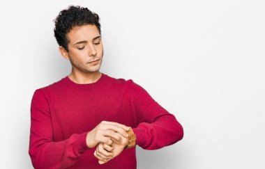 Rahat ve kendinden emin genç, gündelik giysiler giymiş, saati kol saatine göre kontrol eden yakışıklı bir adam. 