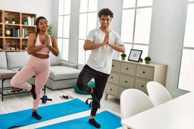 Gülümseyen genç Latin çift evde mutlu yoga pozu veriyor..