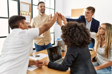 Bir grup işçi ofiste el ele kutlama yaparken gülümsüyor..