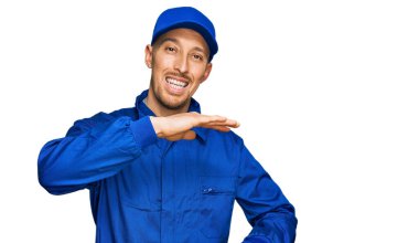 Kel, sakallı, inşaatçı tulumu giyen, elleri büyük ve büyük boy işareti gösteren, ölçü sembolü olan bir adam. Kameraya bakıp gülümsüyor. ölçüm kavramı. 