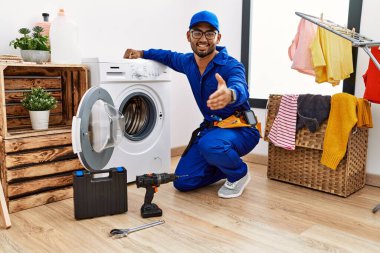 Çamaşır makinesinde çalışan genç Hintli teknisyen dostça gülümseyerek selamlama ve hoş geldin diyor. başarılı iş. 