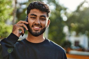 Genç Arap adam gülümsüyor. Parktaki akıllı telefondan konuşuyor.