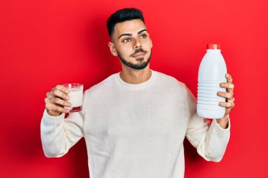 Sakallı, elinde bir bardak süt ve plastik şişeyle gülümseyen ve kafasını çeviren genç bir İspanyol.. 