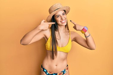Bikini giyen, yaz şapkalı neşeli gülümseyen, parmaklarıyla ve ağzıyla işaret eden İspanyol bir kadın. diş sağlığı kavramı. 