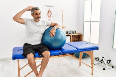Orta yaşlı İspanyol bir adam ağrı kesici kliniğinde elinde pilates topu tutuyor ve soru soruyor. Şüpheyle kararsız, kafa kafaya düşünerek. Düşünceli kavram. 