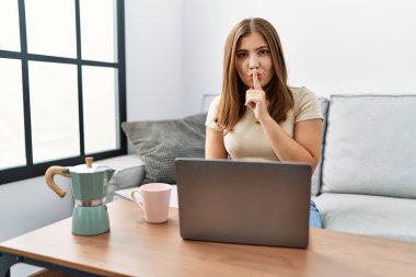 Genç esmer kadın evde dizüstü bilgisayar kullanıyor bir fincan kahve içiyor ve sessiz olmak istiyor. sessizlik ve gizli konsept. 