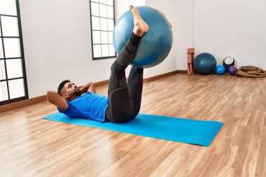 Yakışıklı İspanyol adam egzersiz yapıyor ve yoga minderinde geriniyor, spor salonunda pilates topuyla esneklik gösteriyor.