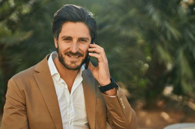 Genç İspanyol işadamı gülümsüyor. Şehirdeki akıllı telefondan mutlu bir şekilde konuşuyor..