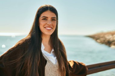 Genç İspanyol kadın gülümsüyor mutlu bir şekilde sahildeki korkuluklara yaslanıyor..