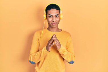 Genç Afro-Amerikalı adam müzik dinlerken kulaklık takıyor ve parmaklarını çapraz yapıp gülümsüyor rahat ve neşeli. Başarı ve iyimserlik 