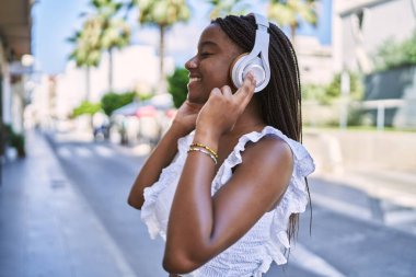 Genç Afrikalı Amerikalı kız gülümseyerek şehirde müzik dinlemekten mutlu oluyor..