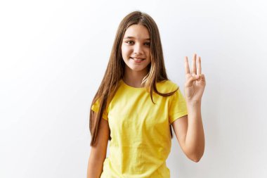 Genç esmer kız izole edilmiş arka planda yan yana duruyor. Üç numaralı parmaklarıyla işaret ediyor ve gülümsüyor. Kendinden emin ve mutlu.. 